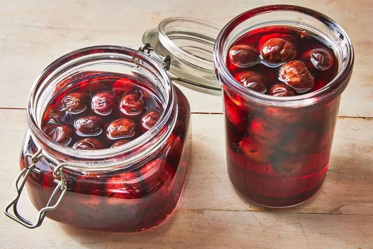 two jars filled with red liquid sitting on top of a wooden table next to each other