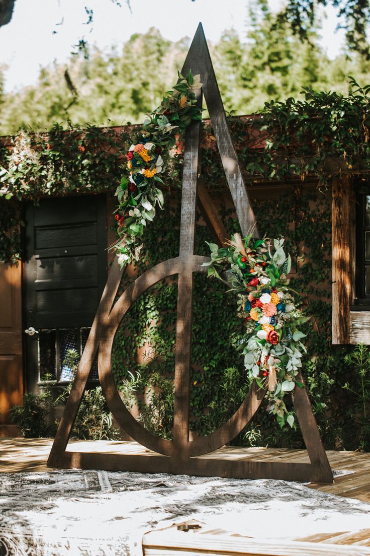 a wooden sculpture with flowers on it in front of a wall covered in greenery