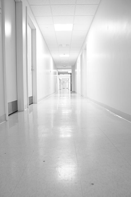 an empty long hallway with white walls and doors on both sides, leading to another room