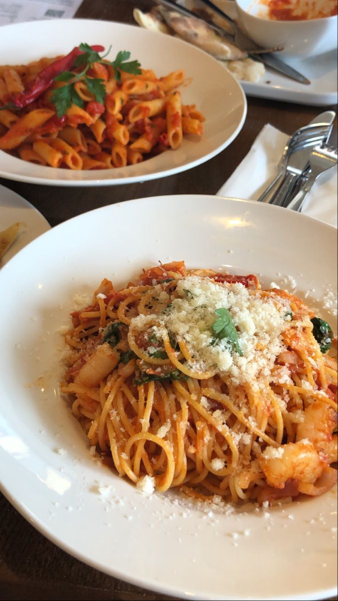 two plates of pasta with sauce and parmesan cheese on the top, along with silverware