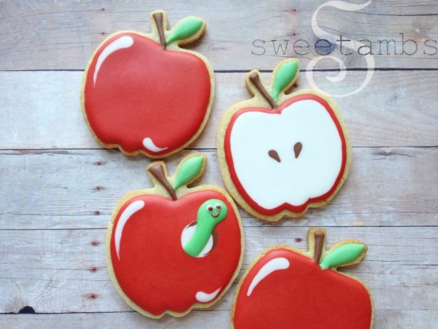 three decorated apple cookies sitting on top of a wooden table