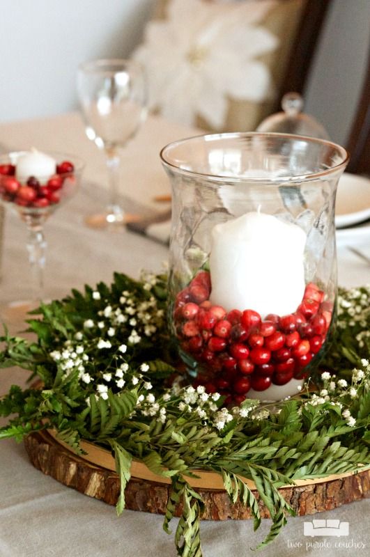 a candle is sitting in a glass bowl on a table with greenery and berries