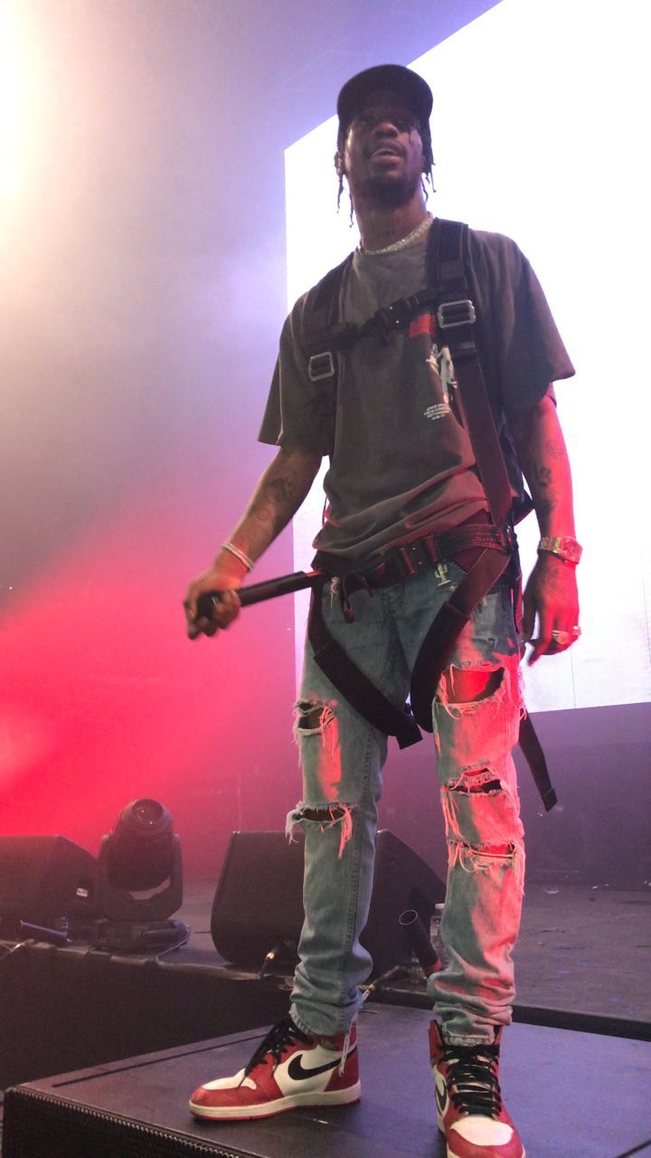 a man standing on top of a stage with a microphone in his hand and wearing ripped jeans