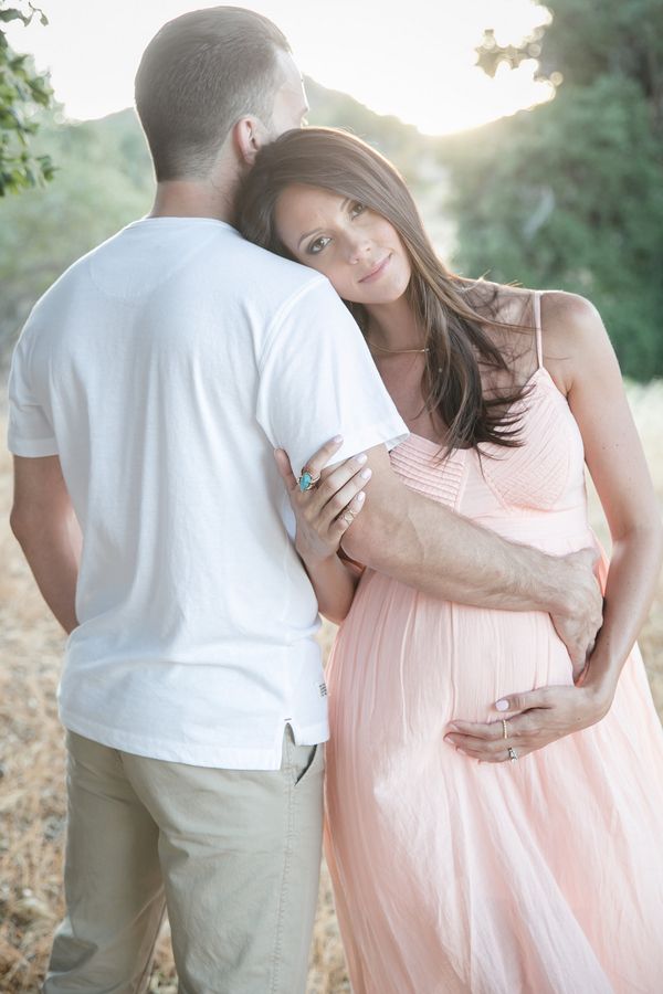 a pregnant woman in a pink dress standing next to a man with his arm around her belly