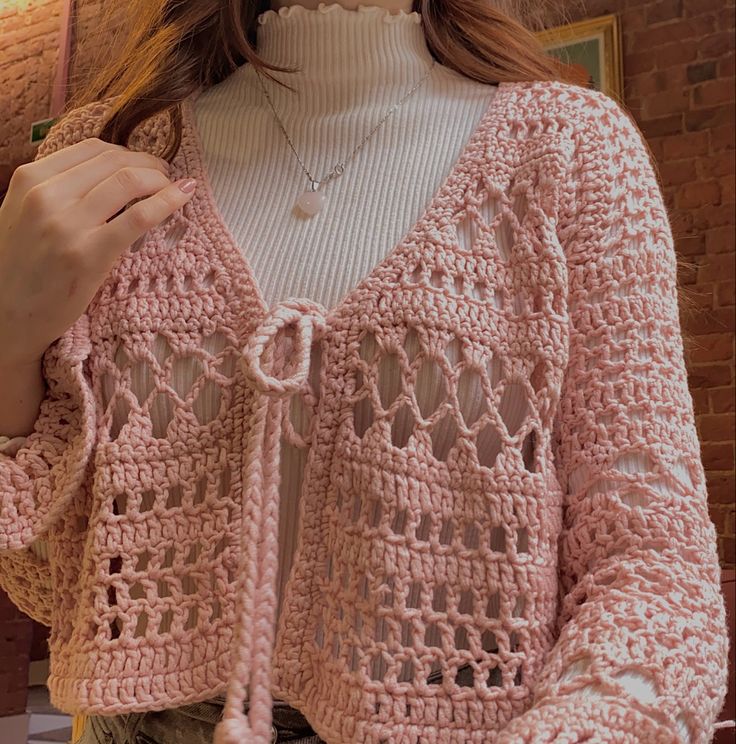 a woman is wearing a pink crocheted sweater