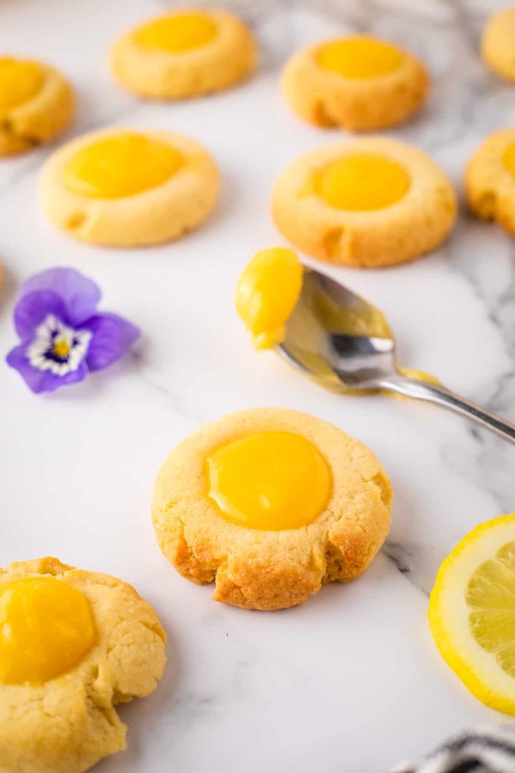 lemon cookies are arranged on a marble surface with purple pansies in the foreground