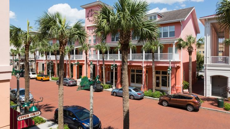 several cars parked on the street in front of pink buildings with palm trees and balconies