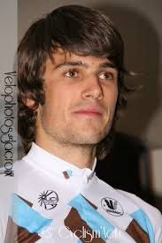 a man with long hair wearing a blue and brown striped shirt looking at the camera