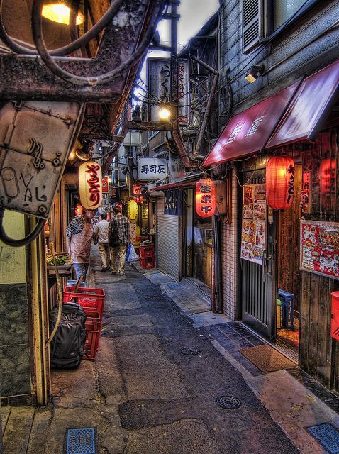 an alley way with people walking down it and signs hanging from the buildings on both sides