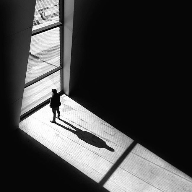 a person standing in front of a window with their shadow on the wall and floor