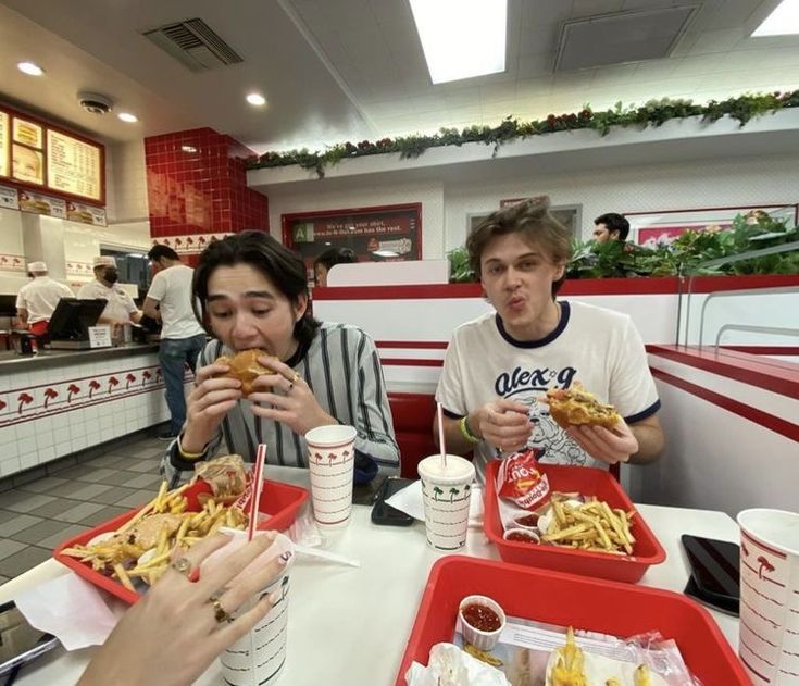 two people sitting at a table with trays of food and drinks in front of them