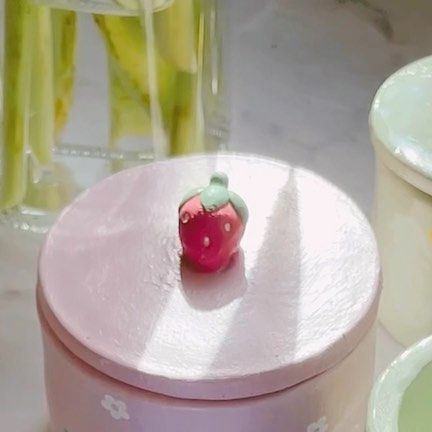 a small strawberry sitting on top of a pink box next to other containers and vases