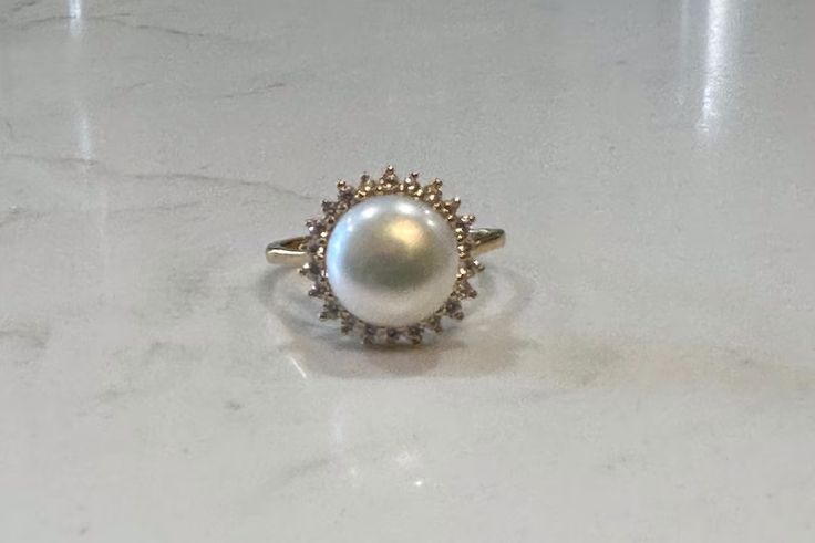 Cleopatra, Princess Di, Jackie O - all loved pearls. The classic gem for classic beauties. This stunning ring features a freshwater pearl encircled by lustrous crystals. Available in silver or gold. Adjustable, size 5-8 PRODUCT DETAILS: 10mm AAA freshwater button iridescent pearl Luster - High Setting: sterling silver or 14kt gold plated with crystal mount Size: Adjustable, Size 5-8 Materials: Freshwater Pearl and .925 sterling silver coated in rhodium or 14kt gold plated over .925 sterling silver Diamond Pearl Ring With Halo For Gift, Pearl White Rings With Pearl Charm For Anniversary, Anniversary Rings In Pearl White With Pearl Charm, Anniversary Pearl White Rings With Pearl Charm, Heirloom Round Pearl Drop Jewelry, Formal Round Cut Halo Pearl Ring, Timeless Pearl Ring With Gemstone, Diamond Pearl Ring With Pearl Drop, Yellow Gold Pearl Ring With Halo