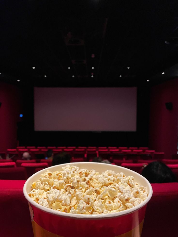 a red bucket filled with popcorn sitting on top of a table in front of a movie screen