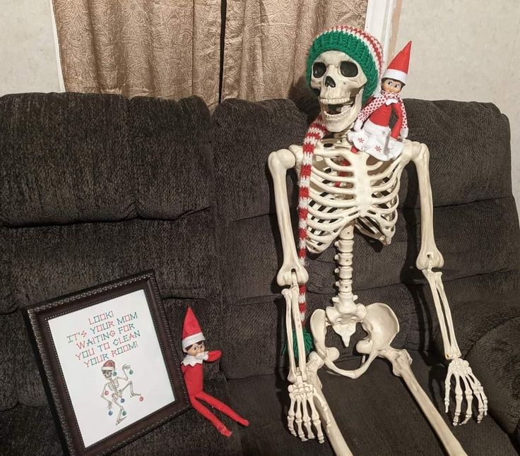 a skeleton sitting on top of a couch next to an elf's christmas hat