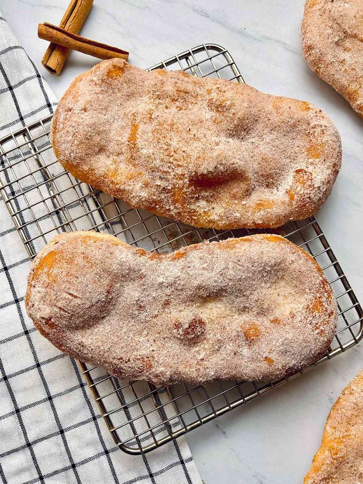 cinnamon sugar doughnuts cooling on a wire rack with cinnamon sticks next to them