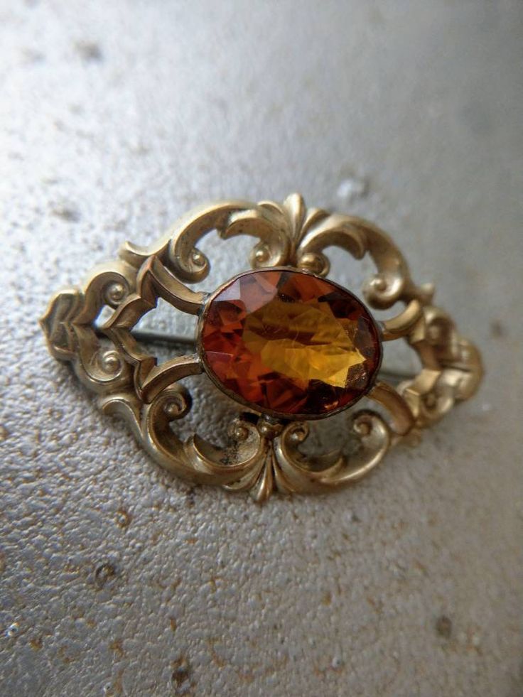 A stunning antique brooch in gold tone metal, possibly gold plated. It is set with a beautiful central orange glass stone, which is reminiscent of a citrine. In good condition, with traces of use due to its age. The stone moves a little bit, but is secure. A few surface scratches on the stone. The brooch measures about 4,8 x 3,7 cm. The stone measures 1,9 x 2,8 cm. Victorian Yellow Gold Brooches With Gemstone, Collectible Gold Brooches With Gemstones, Formal Gold Gemstone Brooches, Antique Gold Brooch With Gemstone, Antique Gold Gemstone Brooch, Antique Yellow Gold Brooches With Gemstone, Victorian Gold Brooch With Intricate Design, Gold Victorian Brooch With Intricate Design, Antique Yellow Gold Filigree Brooches