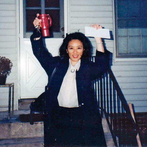 a woman holding up a red cup in front of a white house with her arms raised