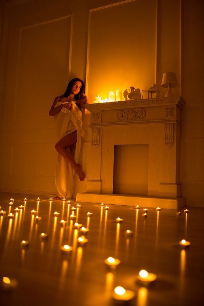 a woman standing in front of a fire place with candles on the floor next to her