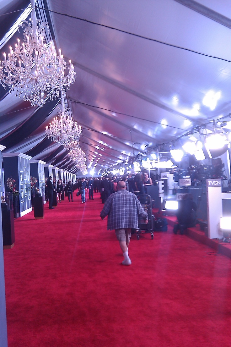 a man walking down a red carpeted hallway with chandeliers hanging from the ceiling