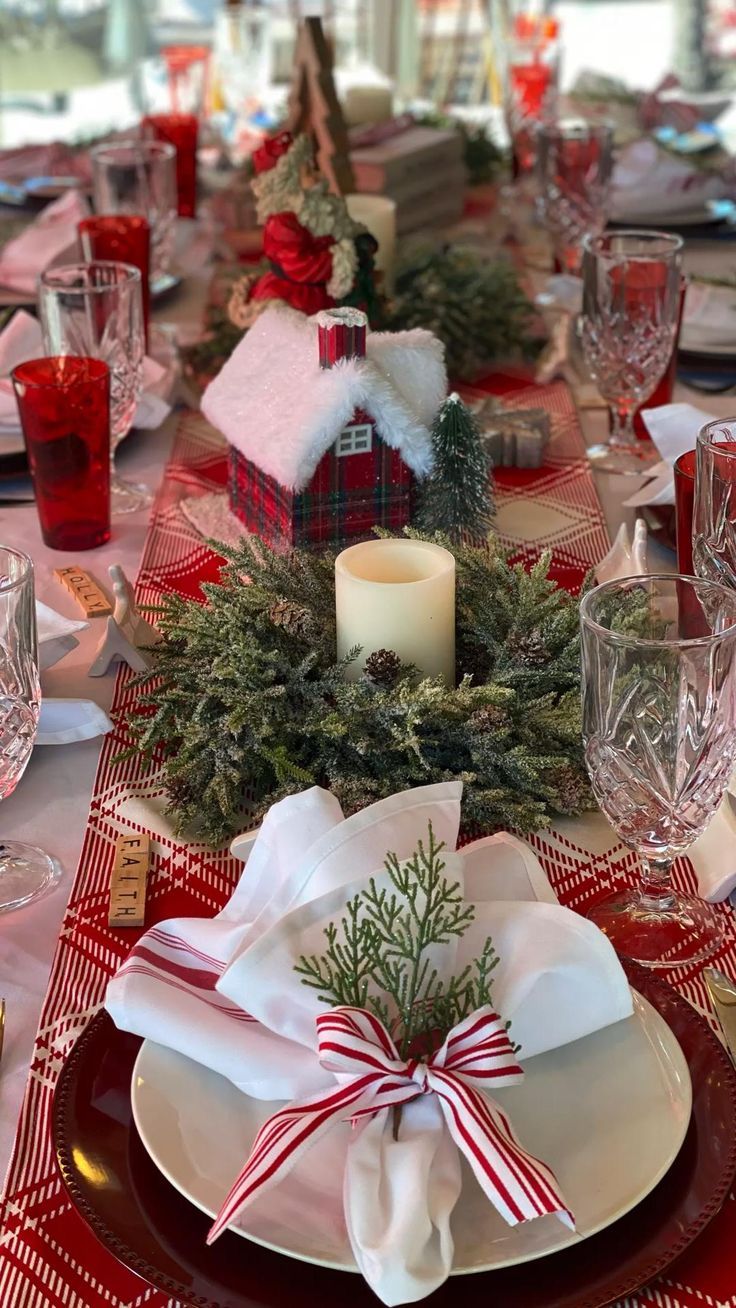 a table set for christmas dinner with red and white plates, napkins, silverware and candlesticks