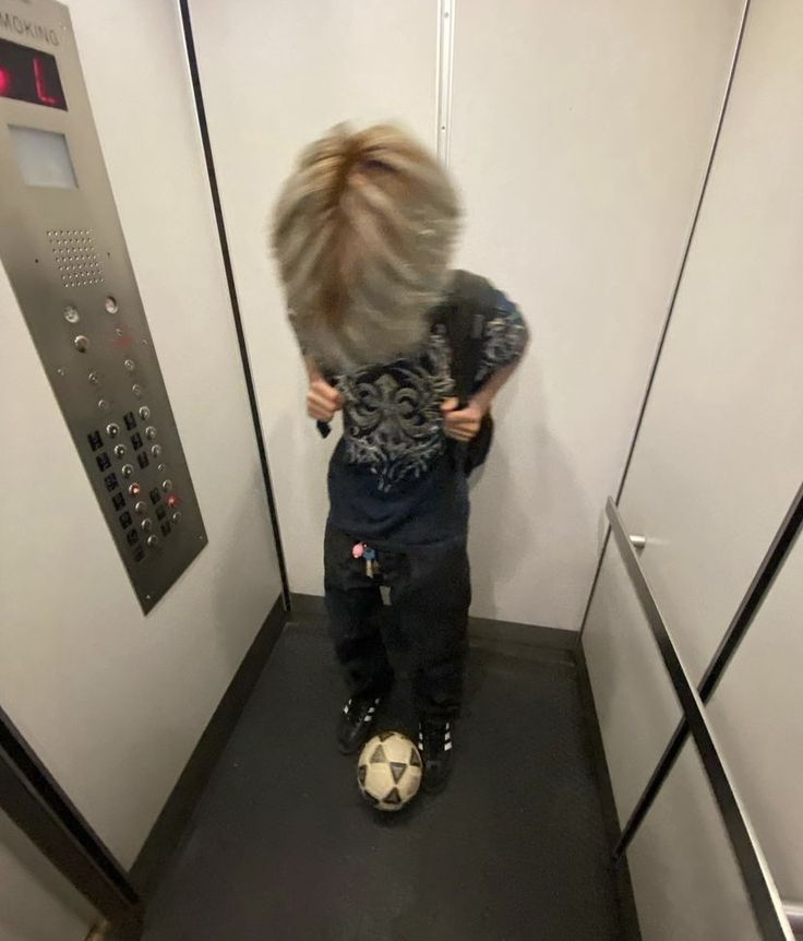 a little boy standing on top of a soccer ball in the corner of a room