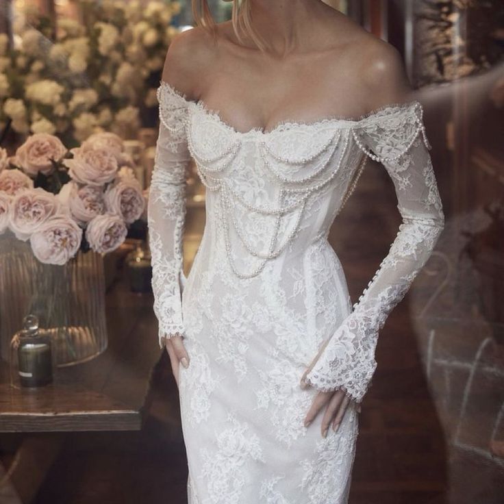 a woman in a white wedding dress standing next to a vase with flowers on it