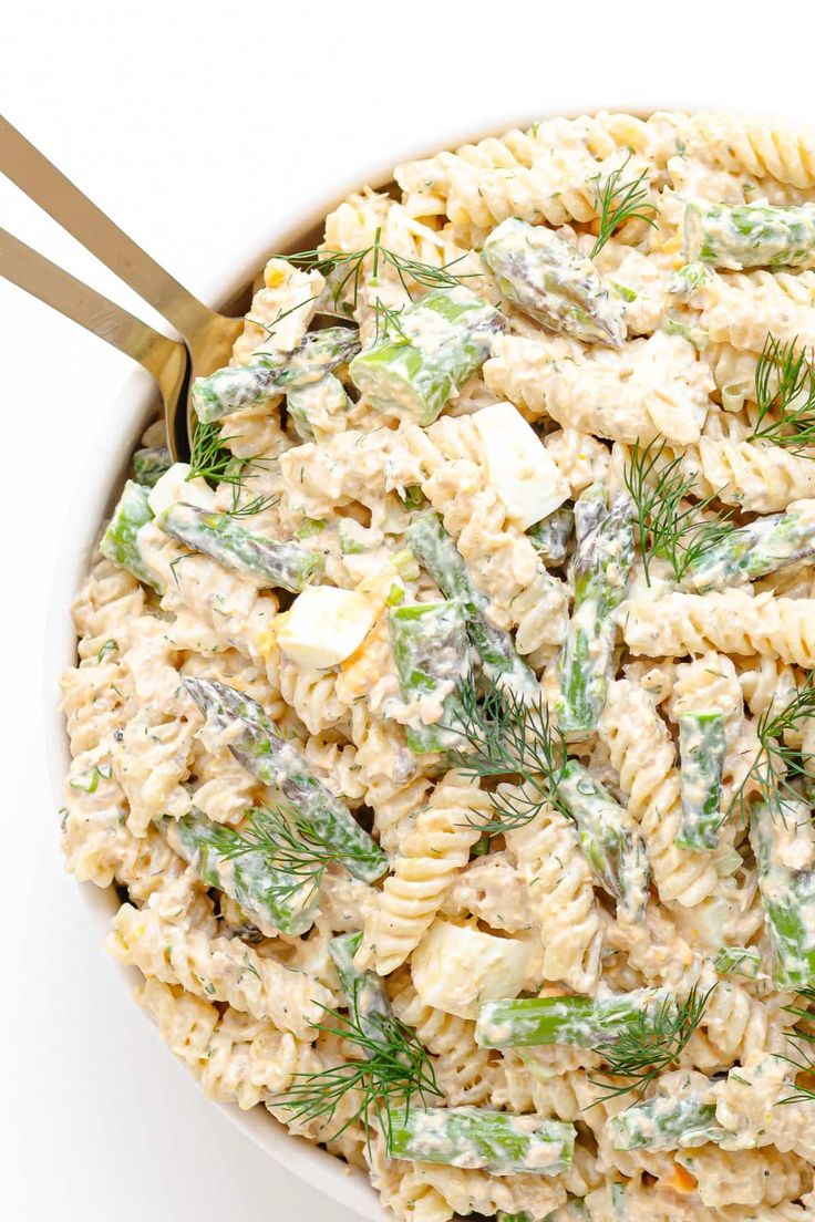 a white bowl filled with pasta salad topped with green onions and dill sprigs