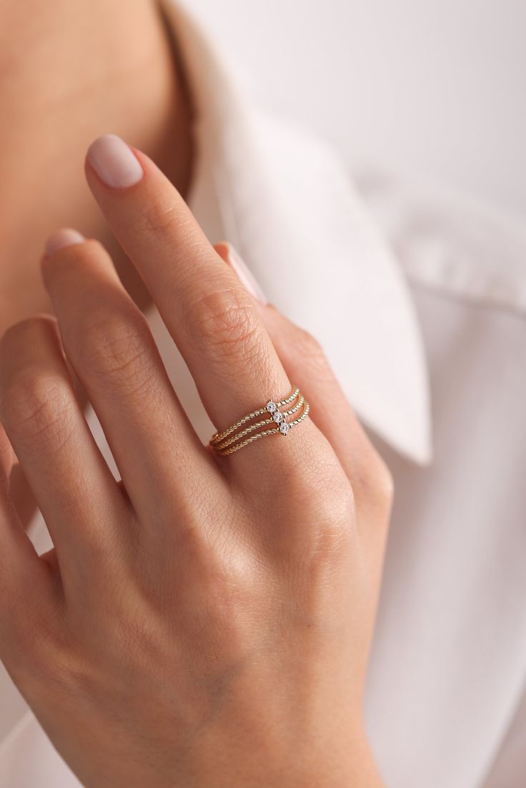 a woman's hand wearing a gold ring with two diamonds on the band and a white shirt