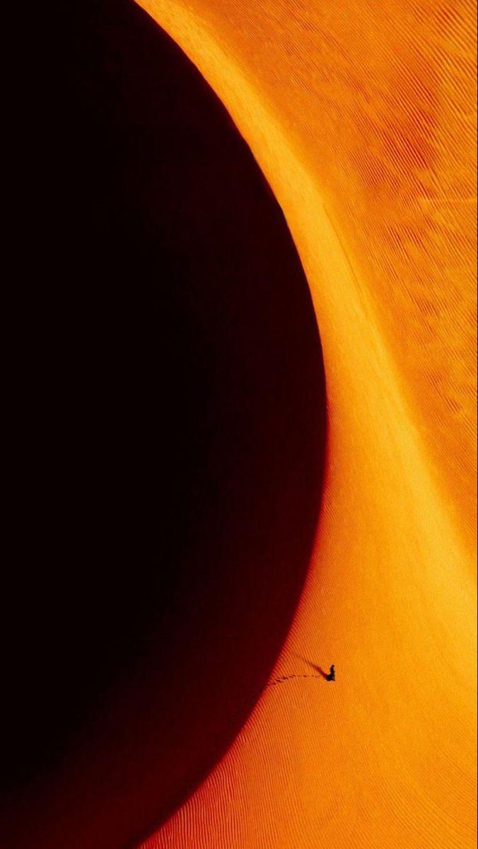 the shadow of a person walking across an orange sand dune