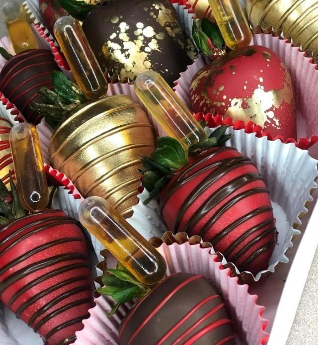 chocolate covered strawberries are in a box with gold foil wrapped around them and some green leaves