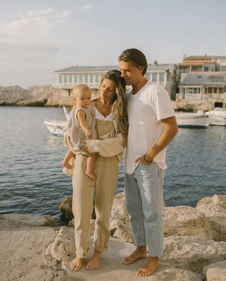 a man, woman and child standing on rocks by the water