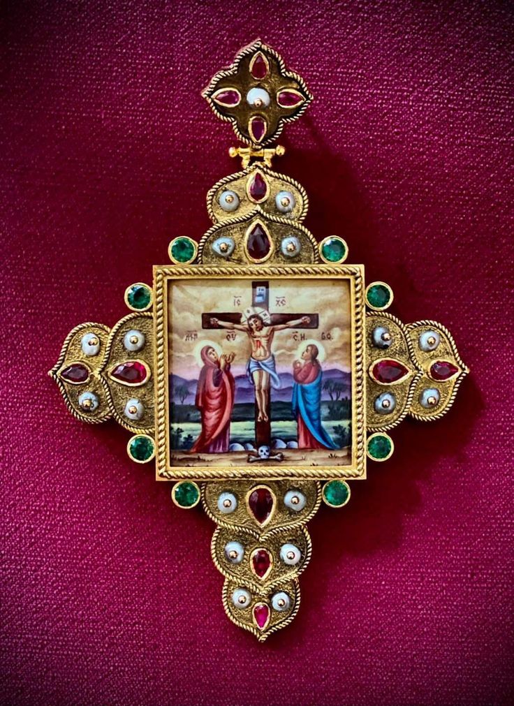 an ornate cross with paintings on it and some stones in the center, sitting on a red cloth