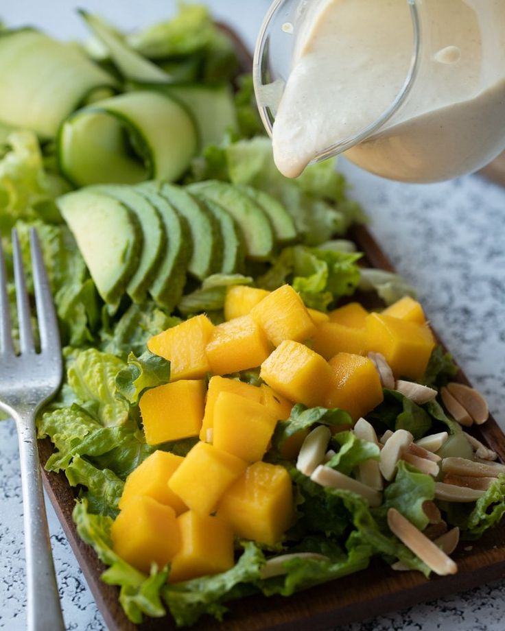 someone pouring dressing onto a salad with avocado and mangoes