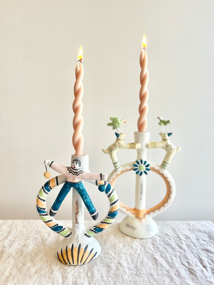 two candles are sitting on a table with some decorations in the shape of people holding hands