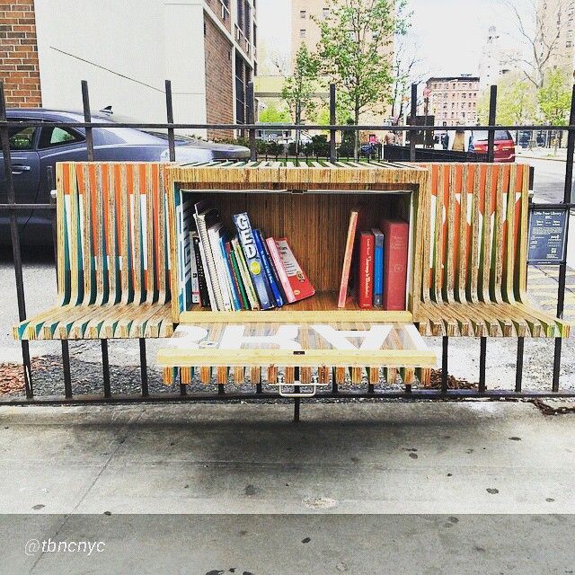 a wooden bench sitting next to a metal fence with books on it and an open book shelf