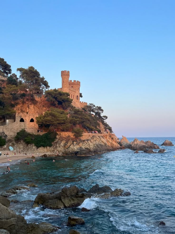 people are swimming in the ocean next to an old castle on a rocky cliff side