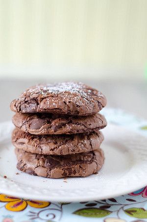 a stack of chocolate cookies sitting on top of a white plate covered in powdered sugar