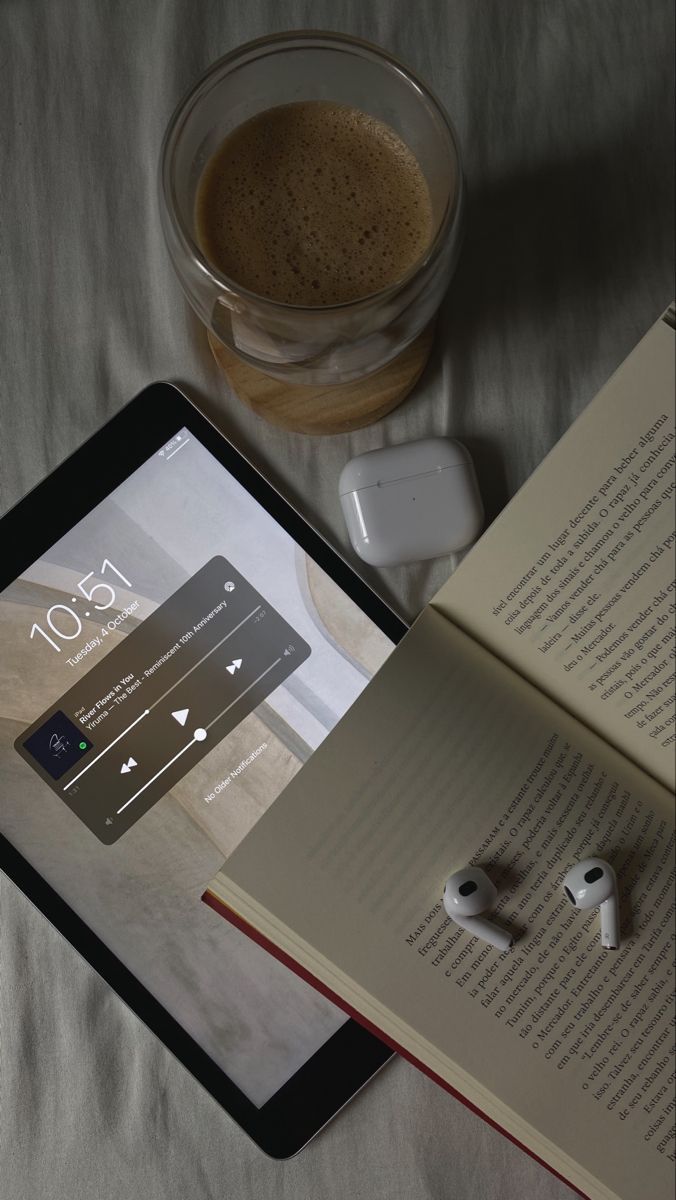 an open book sitting on top of a bed next to headphones and a cup of coffee