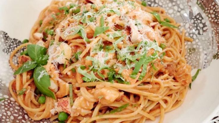 a white plate topped with pasta covered in sauce and greens next to a fork on top of a patterned table cloth