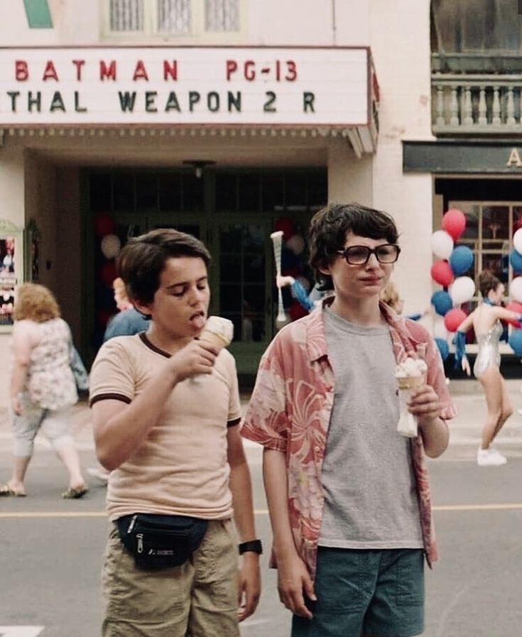 two young boys eating ice cream in front of a movie theater