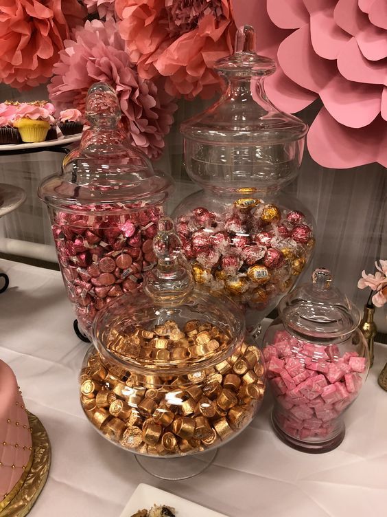 a table topped with lots of pink and gold candies next to cupcakes