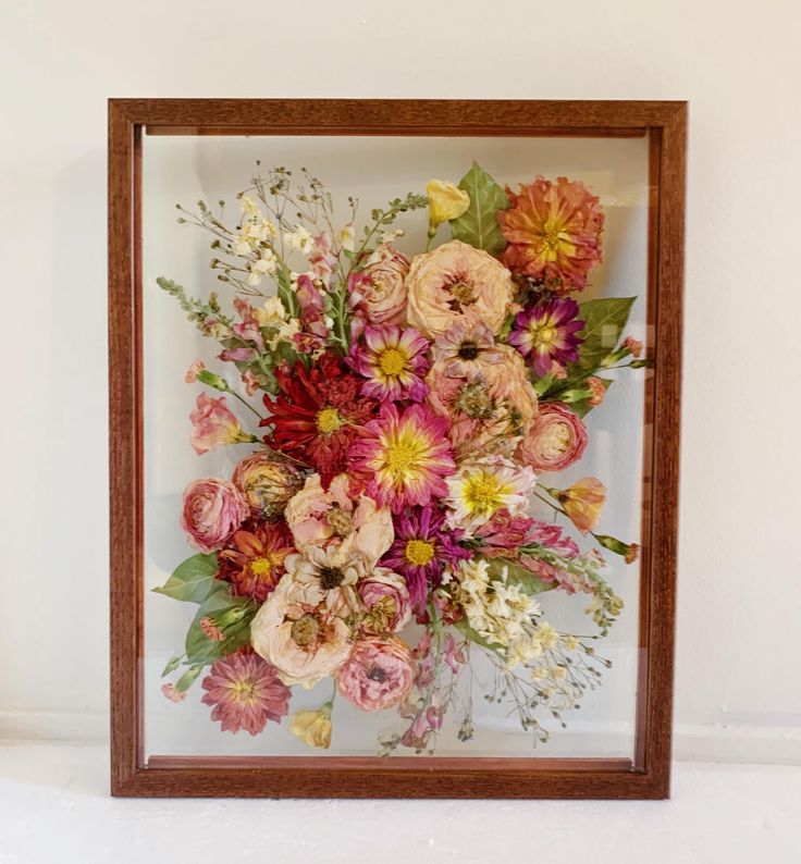 an arrangement of flowers in a wooden frame on a shelf next to a white wall