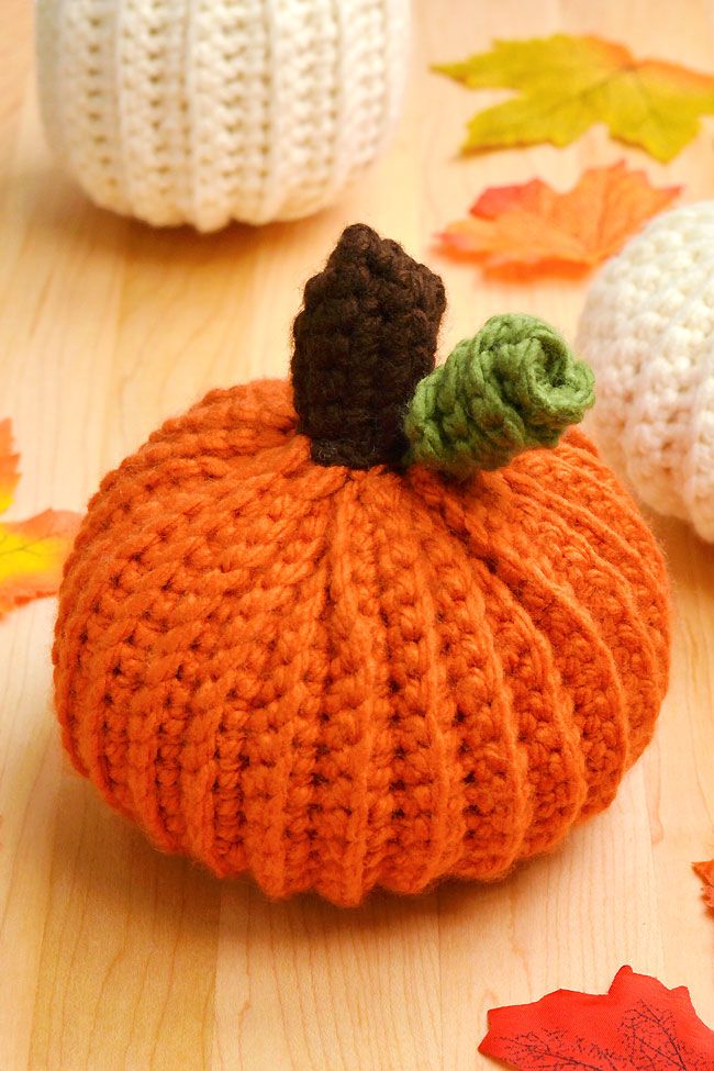 crocheted pumpkins sitting on top of a wooden table with leaves around them