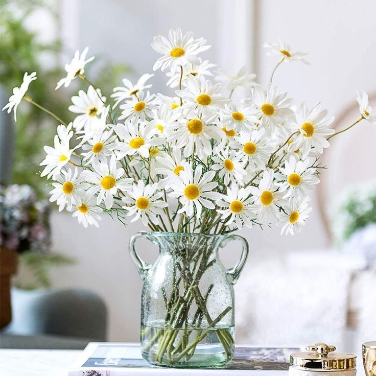 a vase filled with white daisies sitting on top of a table next to a book