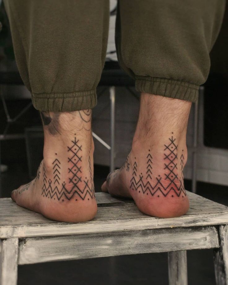 two people with tattoos on their feet sitting on a stool and one has an arrow