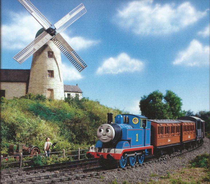 a thomas the tank engine train traveling down tracks next to a windmill on top of a hill