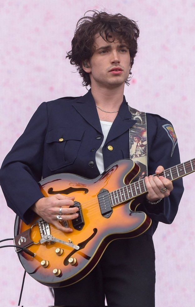 a young man holding an electric guitar in his hands while wearing a blue jacket and black pants