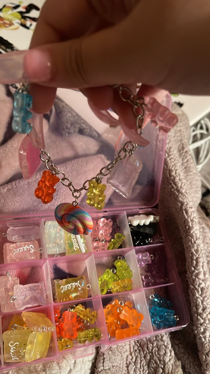 a person is holding a pink box filled with assorted candies and jewelry items