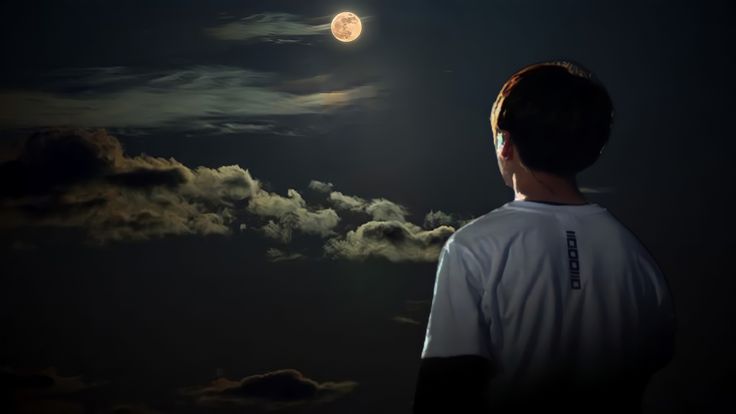 a man is looking at the moon in the night sky with clouds and dark colors